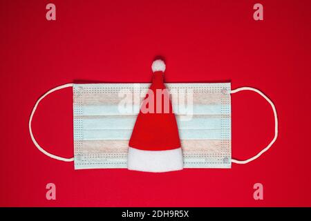 Cappello di Natale su una maschera protettiva del coronavirus. Coronavirus Natale sfondo. Natale o concetto di anno nuovo. Disposizione piatta Foto Stock