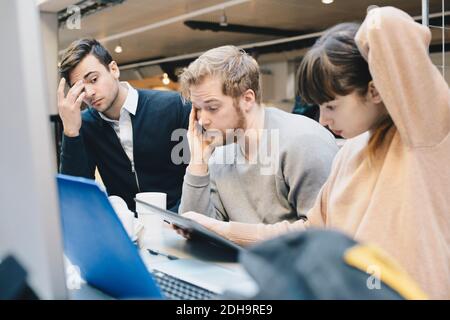 I programmatori di computer che usano il tablet digitale alla scrivania in ufficio sono molto stressati Foto Stock