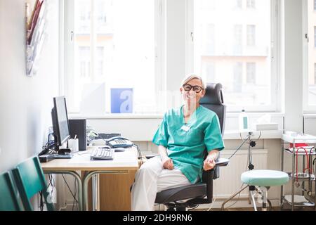 Ritratto di sorridente dottoressa matura seduta in clinica Foto Stock