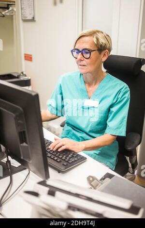 Pediatra femminile che lavora al computer mentre si siede in ospedale Foto Stock