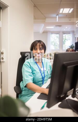 Ritratto di sorridente dottore con bangs che lavorano al computer mentre si siede in clinica Foto Stock