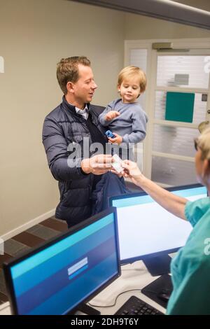 Uomo maturo che dà carta d'identità al medico femminile durante il trasporto figlio in ospedale Foto Stock