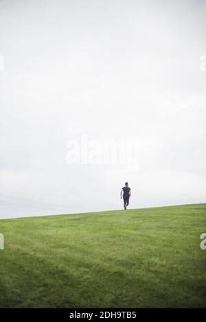 Vista a metà distanza del giovane uomo che corre sul campo contro cielo Foto Stock