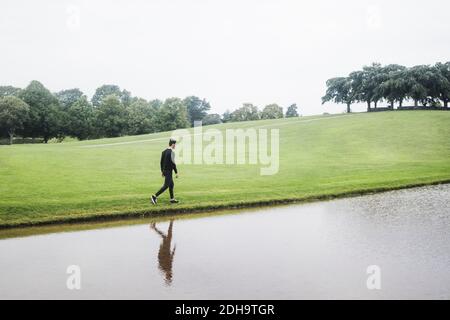 Giovane uomo che cammina lungo il fiume su terra erbosa contro il cielo Foto Stock