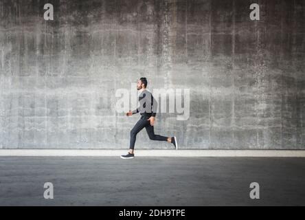 Vista laterale di un giovane uomo che corre da una parete grigia Foto Stock
