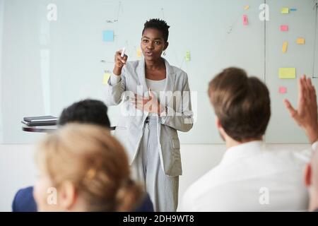 Donna d'affari che indica mentre giovane collega con la mano sollevata seduta dentro seminario in ufficio sul luogo di lavoro Foto Stock