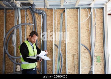 File di lettura di un architetto maschile mentre si è in piedi in cantiere Foto Stock