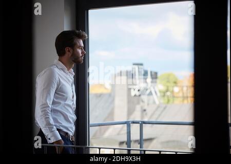 Contemplando l'uomo d'affari che guarda attraverso la finestra mentre si alza dalla finestra dell'ufficio Foto Stock