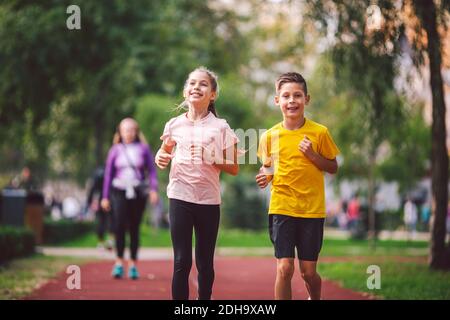 Sport e fitness in adolescenza. I gemelli caucasici, ragazzo e ragazza, corrono sulla pista da jogging nel parco cittadino. Due figli fratello Foto Stock