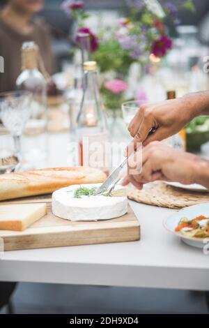 Mani tagliate di uomo che taglia la mozzarella sopra il tagliere a. terrazza dell'edificio durante la festa Foto Stock