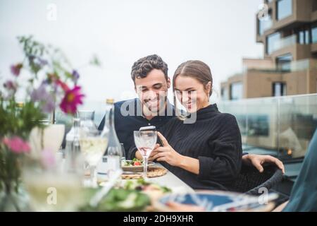 Felici amici di sesso maschile e femminile che usano la fotografia telefonica durante il tetto festa Foto Stock