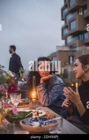 Sorridendo amici donne che parlano mentre si siede sulla terrazza dell'edificio durante tramonto Foto Stock