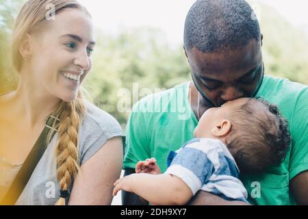 Primo piano di una donna sorridente che guarda l'uomo baciando il figlio Foto Stock