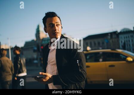 Giovane uomo che guarda via mentre tiene lo smartphone durante la città esplorazione Foto Stock