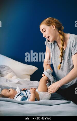 Madre che parla sul telefono cellulare mentre vestiva il bambino a. casa Foto Stock