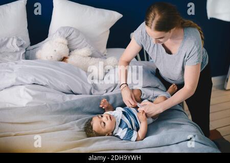 Madre vestendo bambino ragazzo a letto a casa Foto Stock