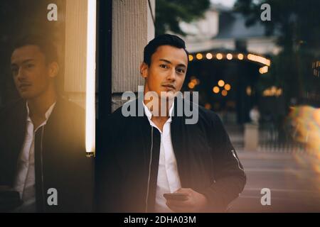Ritratto di giovane uomo con telefono in piedi in città Foto Stock