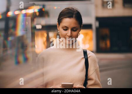 Giovane donna che usa il telefono mentre si trova in città Foto Stock