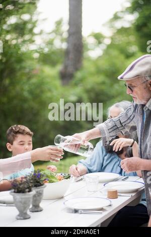 Uomo anziano che versa acqua per la donna nel cortile posteriore Foto Stock