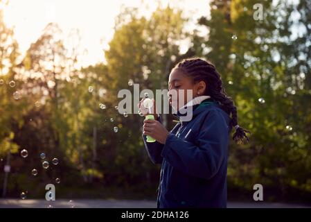 Vista laterale della ragazza che tiene la bacchetta della bolla contro gli alberi a. campeggio Foto Stock