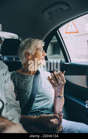 Donna anziana che tiene lo smartphone mentre si è seduti in auto durante vacanza Foto Stock