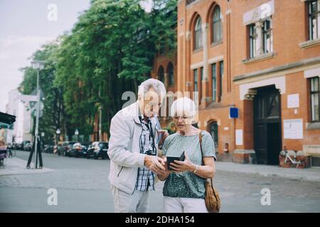 Donna anziana che tiene uno smartphone che discute con il partner durante l'esplorazione in città Foto Stock