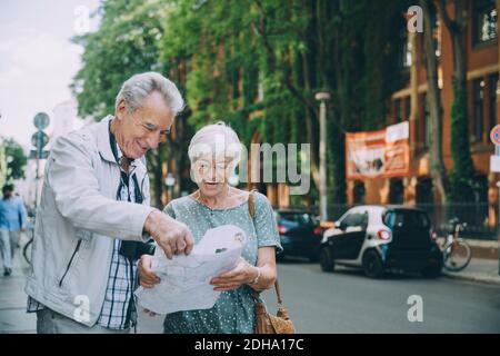 Una coppia sorridente anziana che legge la mappa mentre si è in piedi sul marciapiede dentro città durante le vacanze Foto Stock