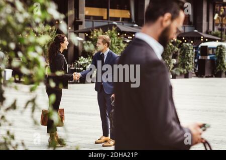 Imprenditori maschili e femminili scuotono le mani mentre si levano in piedi all'aperto Foto Stock