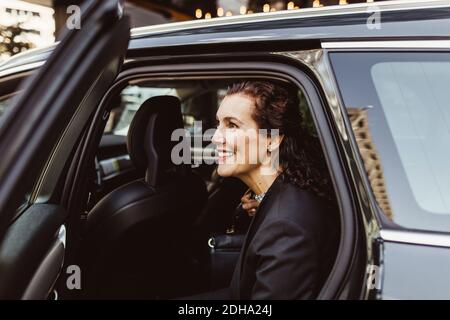 Sorridente imprenditore femminile che guarda via mentre esce dalla macchina Foto Stock