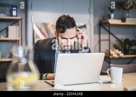 Giovane uomo d'affari che lavora su un computer portatile mentre si siede al tavolo ufficio Foto Stock