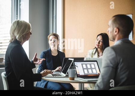 Donna d'affari anziana che discute le strategie con i colleghi mentre siede a bordo camera Foto Stock