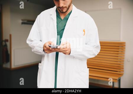 Sezione centrale del giovane medico che usa lo smartphone nel corridoio dell'ospedale Foto Stock