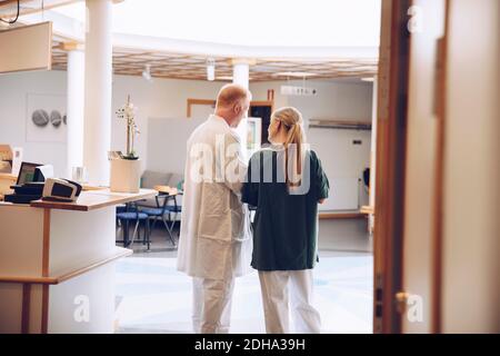 Vista posteriore dell'infermiera femminile e del medico di sesso maschile che discutono mentre in piedi nella lobby dell'ospedale Foto Stock