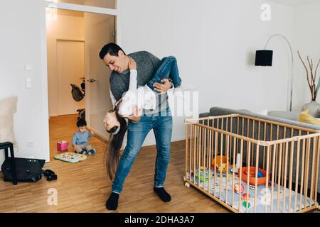 Tutta la lunghezza del padre giocoso che solleva la sua figlia mentre il figlio giocare con i giocattoli in soggiorno Foto Stock
