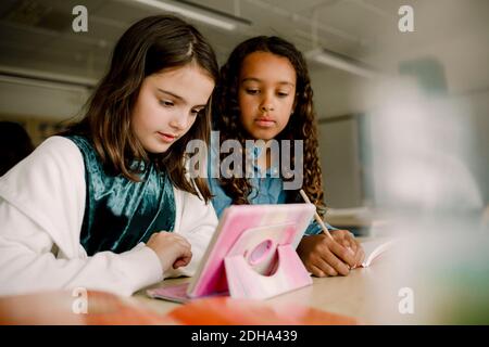 Studenti di sesso femminile che usano il tablet digitale al tavolo in classe Foto Stock