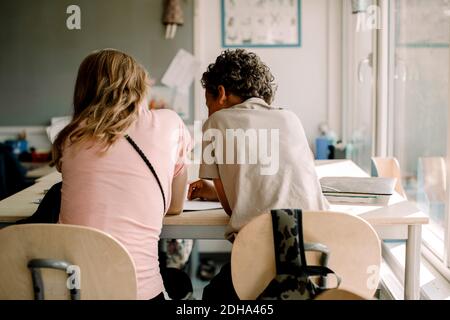 Vista posteriore di studenti di sesso maschile e femminile che studiano insieme in aula Foto Stock