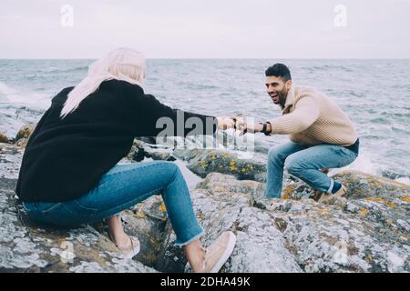 Giovane donna che passa telefono cellulare a uomo su rocce a. spiaggia Foto Stock