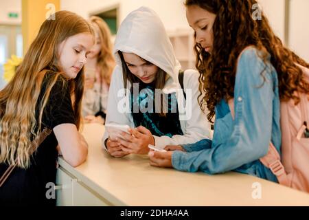 Le studentesse che usano il telefono mentre si levano in piedi nel corridoio della scuola durante pausa pranzo Foto Stock