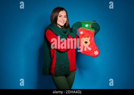 Foto di affascinante bella ragazza giovane tenere fiocchi di neve cervi ornati calza preparare segreto di famiglia presente indossare rosso pullover sciarpa verde guanti Foto Stock