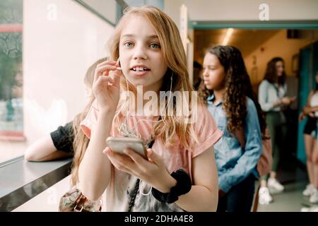 Studentessa che parla con le cuffie intrauricolari nel corridoio scolastico Foto Stock