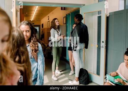 Studenti junior in piedi accanto alla porta nel corridoio scolastico Foto Stock