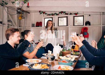 Amici felici maschi e femmine che alzano gli occhiali da vino in cottage Foto Stock