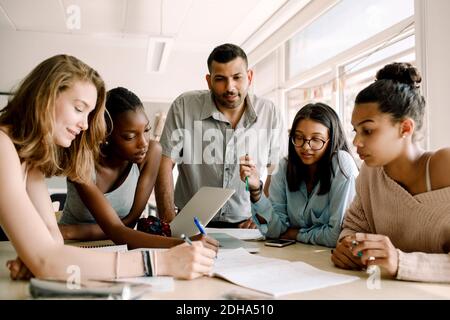 Adolescenti donne che studiano mentre professore in piedi da tavolo in classe Foto Stock