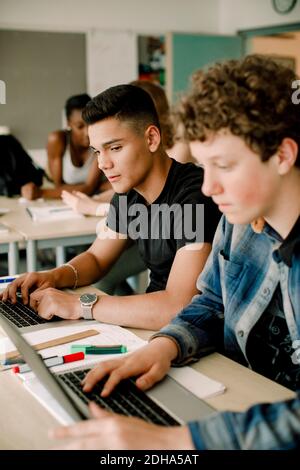 Gli studenti maschi che usano il computer portatile mentre si siedono al tavolo in classe Foto Stock