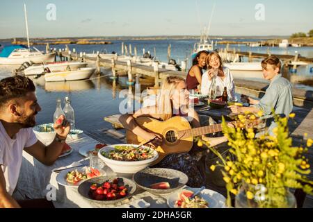 Amici che ascoltano una donna che suona la chitarra in festa al porto Foto Stock