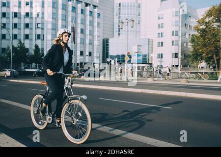 Tutta la lunghezza della giovane donna che indossa il casco in bicicletta via in città Foto Stock