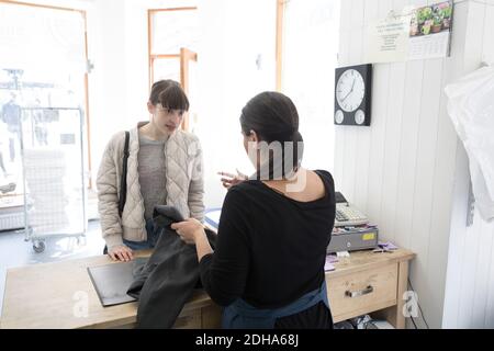 Vista posteriore di una donna matura proprietario Laundromat che parla con i giovani cliente al momento del pagamento Foto Stock