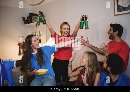 Donna allegra che tiene le bottiglie di birra in piedi con gli amici nel vivere camera Foto Stock