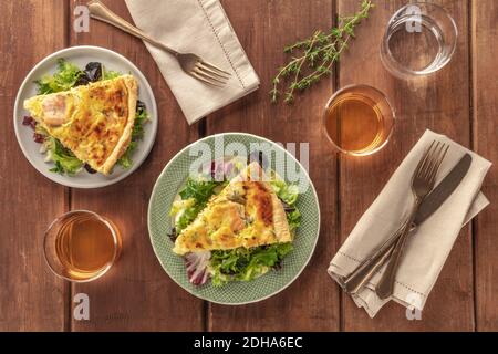 Fette di quiche francesi con salmone, con foglie di insalata verde, timo e vino bianco, sparate dall'alto su un rustico backgro di legno Foto Stock