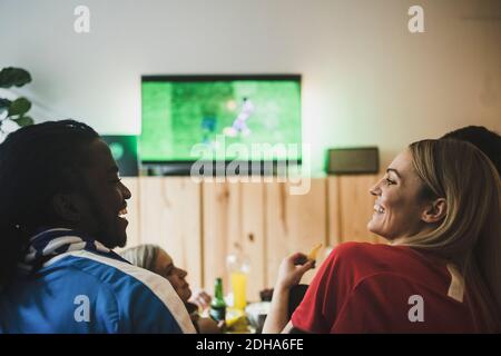 Sorridendo maschio e femmina guardando il calcio mentre si siede con gli amici a casa Foto Stock